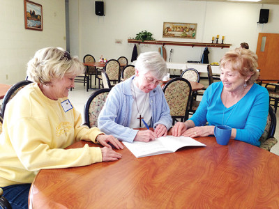 Sister Dorothy Ann Balser signs a copy of her book, “Bitsy Bee with the Allergy” for Mary Parker (left) while Nancy McGee looks on. Sister Balser talked about her book to St. Therese parishioners during their annual retreat at St. Mary of the Pines. (Photo by Elsa Baughman)
