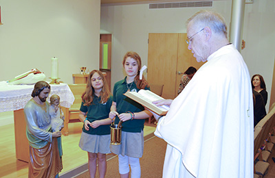 Father Bill Henry blesses the antique statue of St. Joseph in the school chapel with help from 