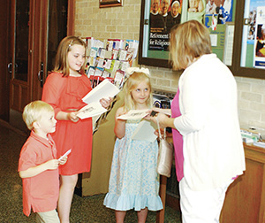 Andrew, Sarah Beth and Sophie Johnston, the deacon's nephew and nieces, hand out prayer cards before the liturgy. (Photos by Maureen Smith)