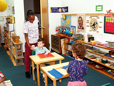 Maxine Kinnard, Montessori teacher, helps Josiah L. get settled while Edith R. watches. Some of the children in the program are second generation attendees. 