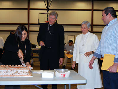 Lupita Hernández corta un pedazo del pastel para el obispo mientras la Hermana Josefina García e Ivan Varelan observan. (Fotos de Elsa Baughman)