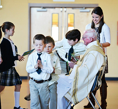 Msgr. Michael Flannery receives farewell cards from St. Anthony School students after celebrating Mass at the school. He retired in January and is working for the Tribunal, helping with annulments. (Photo by Dave Vowell)