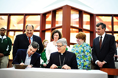 Bishop Joseph Kopacz (center) and (l-r) Paul Artman, St. Joseph High School principal, Michelle Gardiner, principal of Our Lady of Lourdes School, Catherine Cook, superintendent of Catholic Schools, and Aad DeLange, chief financial officer for the diocese, observe Jimmy Carpenter sign the contract of the construction of the new classrooms. (Photos courtesy of Doreen Muzzi) 
