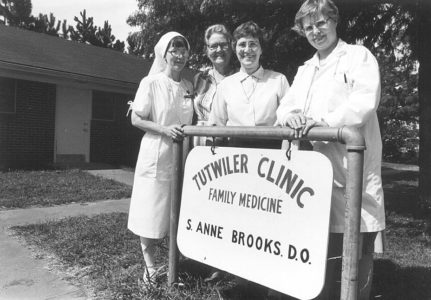 Three Sisters of the Holy Names of Jesus and Mary with Sister Anne Brooks, D.O., stand by the sign on opening day of the Tutwiler Clinic on August 15, 1983. 