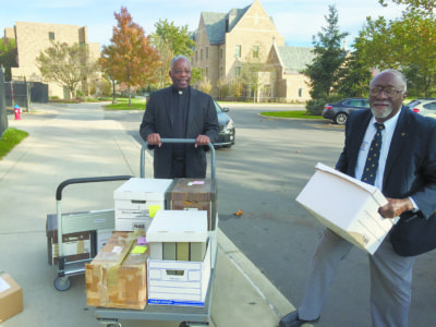 Father Kenneth Taylor, president of the National Black Catholic Clergy Caucus, pushes a cart of archival material earmarked for the Theodore Hesburgh Library on the campus of the University of Notre Dame in South Bend, Ind., Oct. 25. Assisting him is Holy Cross Brother Roy Smith of Notre Dame. (CNS photo/courtesy Catholic African World Network) See BLACK-HISTORY-MONTH-CLERGY Nov. 2, 2016.