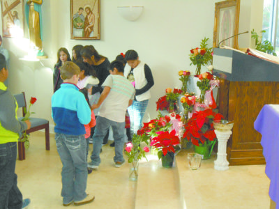 BOONEVILLE – St. Francis of Assisi Parish children gather in front of a newly blessed image of Our Lady of Guadalupe to adorn it with roses Sunday, Dec. 11, during the celebration of her feast day. After Mass parishioners enjoyed a feast of Mexican food and other items during a potluck dinner. (Photo by Sheila Przesmicki) 