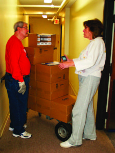 JACKSON – Neil Rhodes chats with Betty Carlyn as he drops off supplemental food boxes at a senior living community in Jackson.  He hopes to recruit more drivers for the monthly ministry. (Photo by Tereza Ma.) 