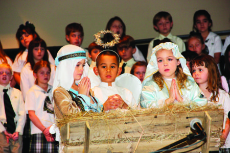 MADISON – To celebrate the Advent Season, St. Anthony students performed their Christmas program for parents, staff, and friends on Monday, Dec. 19. Above, John Charles Camarato, Benedict Jones, and Mamie Heitzmann gaze over baby Jesus. (Photo courtesy of Teresa McMullin.)