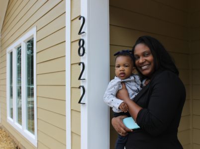 Homeowner Ariel Jones stands in front of her new home with her baby. 