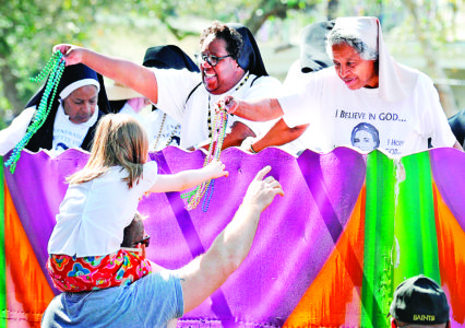 Religious sisters hand beads to a man and child Feb. 19 from the Krewe of Femme Fatale float during a parade in New Orleans. Twenty Sisters of the Holy Family boarded the float, the first time in Mardi Gras history that a women's religious congregation participated as a group on a Carnival float. Over their habits they wore a T-shirt honoring Mother Henriette Delille, who founded their congregation in 1842. (CNS photo/Christine Bordelon, The Clarion Herald) See NEW-ORLEANS-PARADE-SISTERS Feb. 8, 2017.