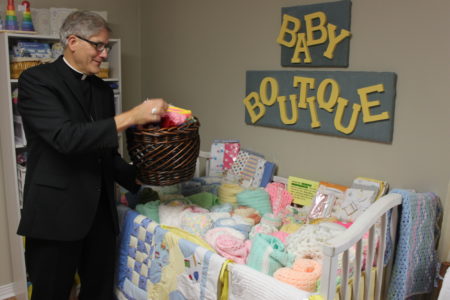  Bishop Joseph Kopacz, inspects hand-made infant blankets and caps in the Baby Boutique while visiting. Infant supplies are earned by clients who attend prenatal and parenting classes. Mothers can exchange points they earn for needed supplies in the Baby Boutique.  Classes are given by volunteer staff at the Center.  (Photo by Gene Buglewicz)